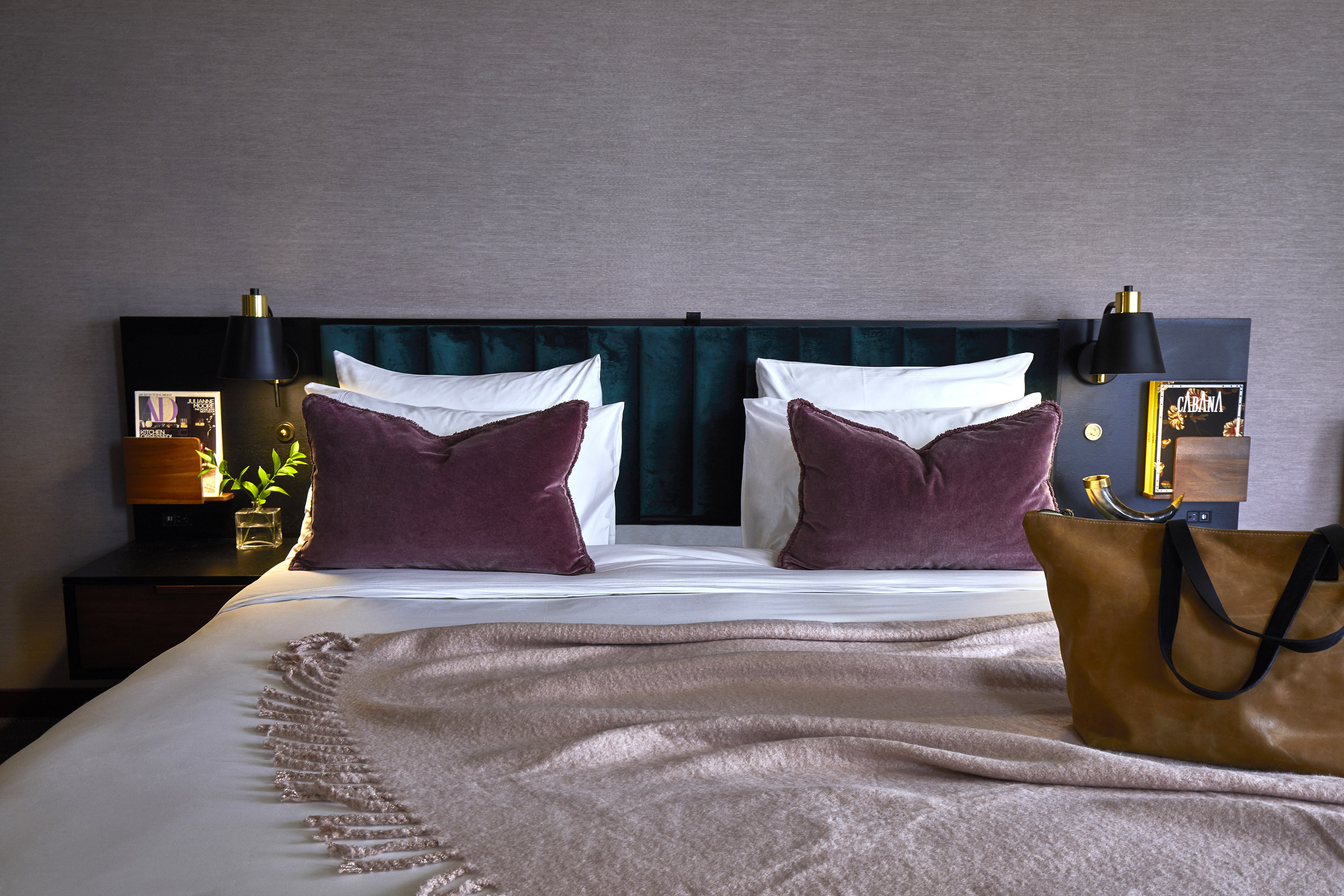 A neatly made bed with a dark green headboard, white pillows, and maroon throw pillows, with a beige blanket at the foot.